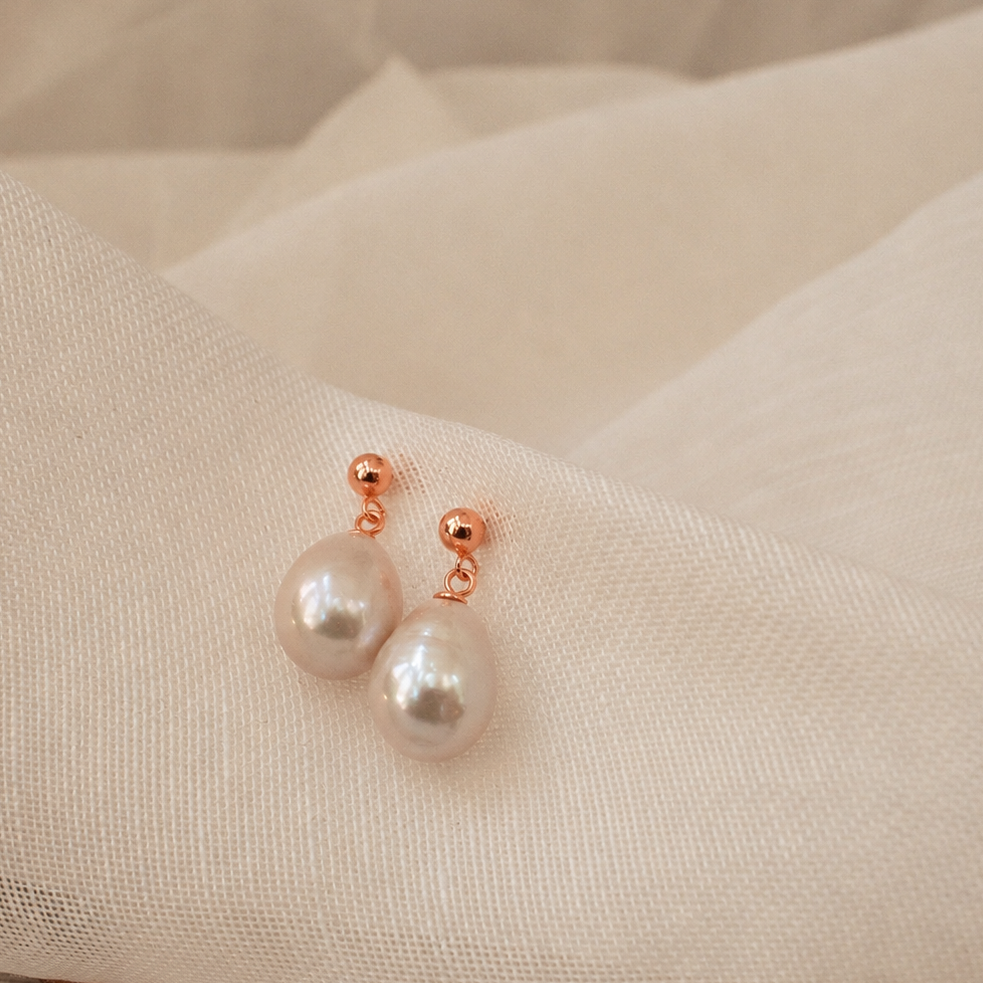Pearl earrings with rose gold posts on a beige fabric background